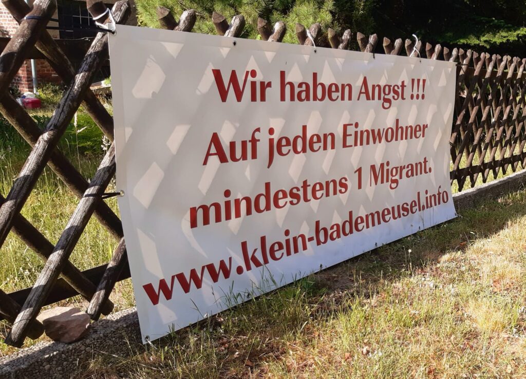 Großes Plakat an einem Gartenzaun mit dem Text: "Wir haben Angst! Auf jeden Einwohner mindestens 1 Migrant. www.klein-bademeusel.ino"